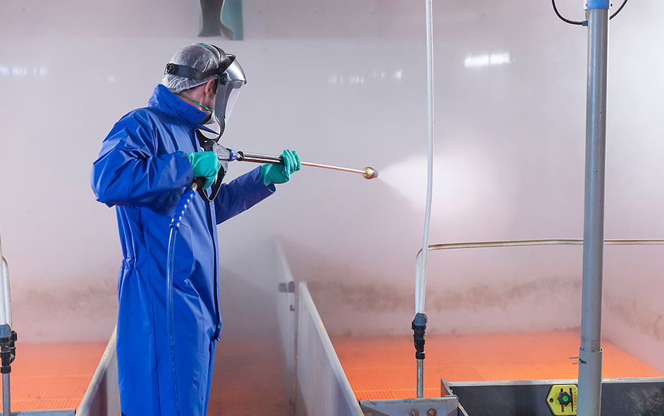 A person in protective gear pressure washing a stall.